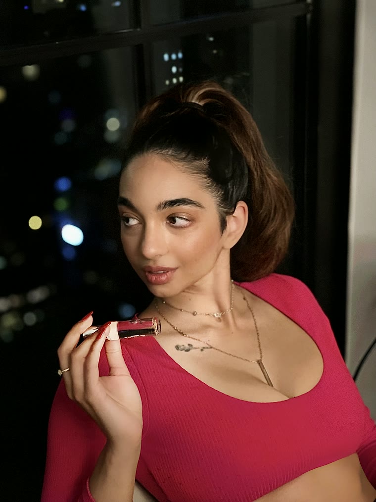 Woman in a pink top holding a Chromelle roll-on perfume oil against city lights at night